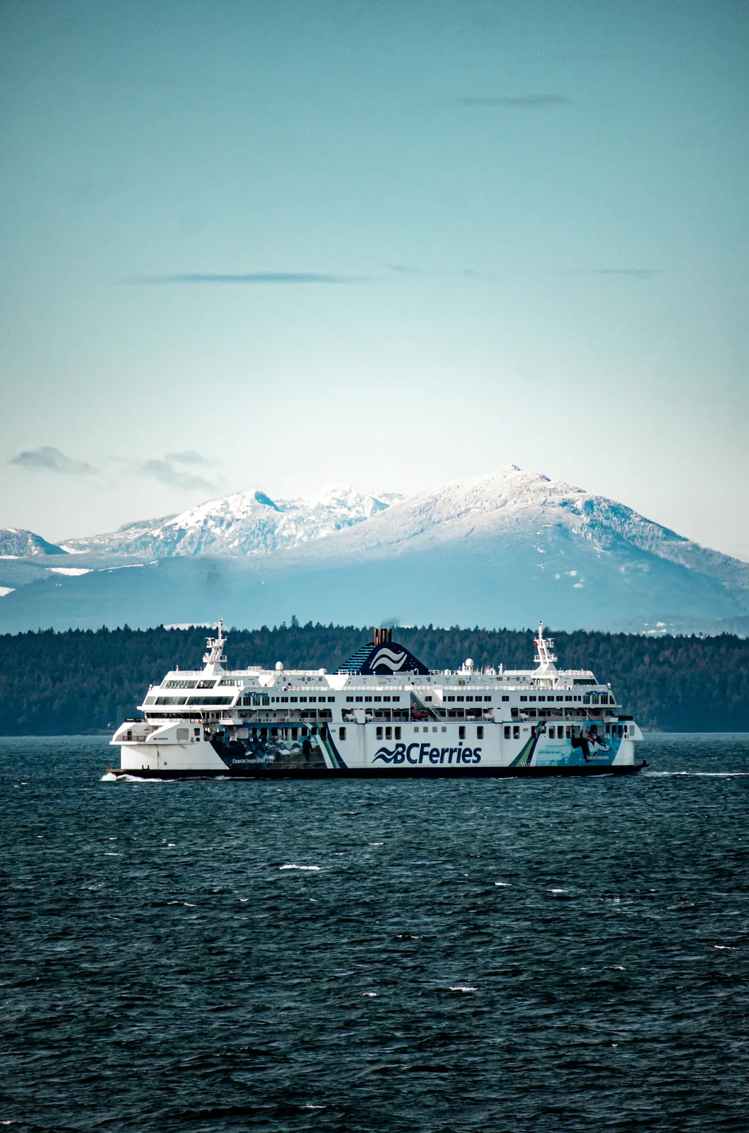 BC Ferries vessel Coastal Inspiration crossing the water with snow-capped mountains behind