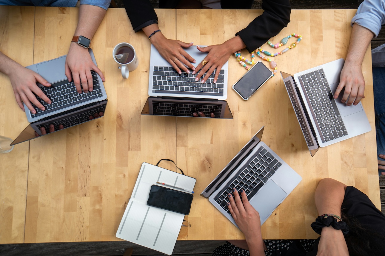 Overhead shot of five communications team members around a table with laptops