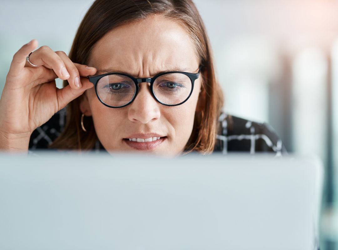 Professional-looking woman peering at a laptop screen looking puzzled and concerned by what she sees.